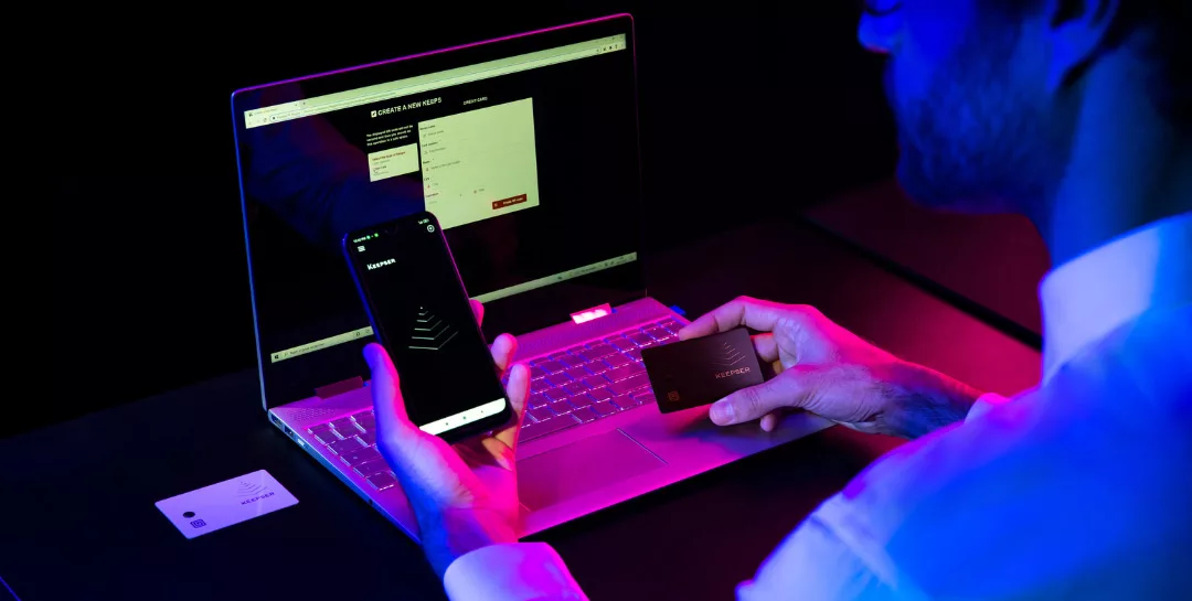 Man using Keepser NFC Cold Wallet with geolocation features on laptop and smartphone.